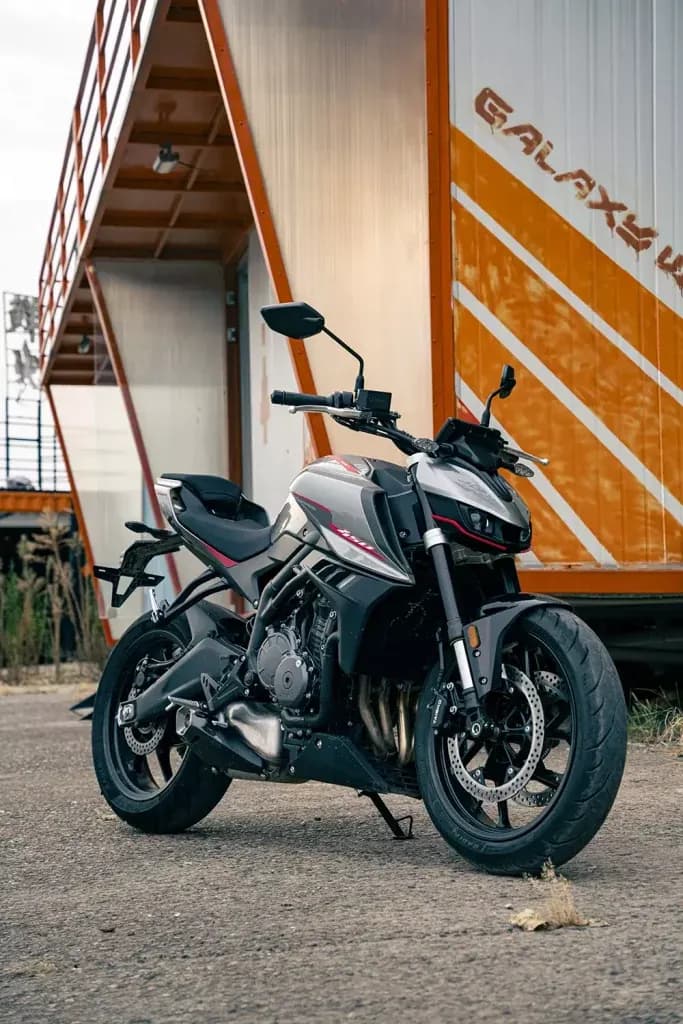 Motocicleta KOVE naked gris plata y negra estacionada sobre asfalto frente a un contenedor blanco y naranja