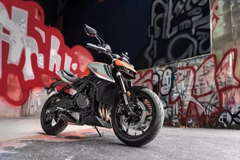 Motocicleta KOVE naked naranja y negra sobre pavimento gris frente a muros cubiertos de grafiti rojo y blanco