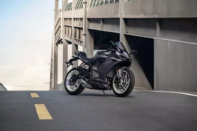 Motocicleta KOVE deportiva de color violeta metalizado estacionada en una vía junto a un gran edificio de hormigón