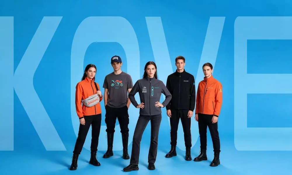 Cinco modelos sobre fondo azul con el logotipo KOVE detrás, vistiendo chaquetas softshell naranjas y grises, camiseta gris, chaqueta negra, gorra azul marino y riñonera gris con logo KOVE