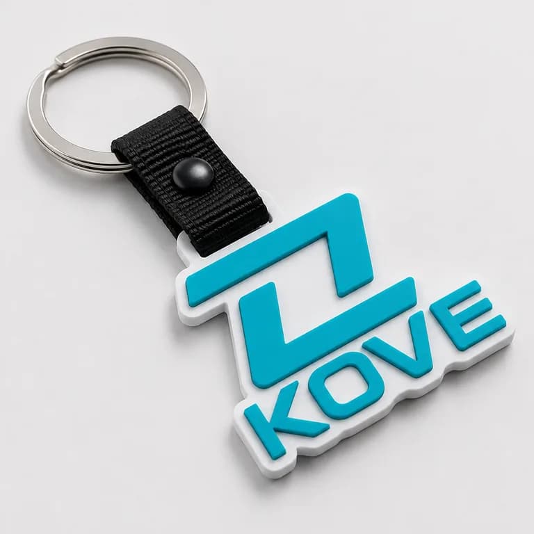 Llavero de caucho con la forma del logotipo KOVE en relieve, en verde agua sobre una base blanca, unido por una correa negra con broche a una argolla metálica