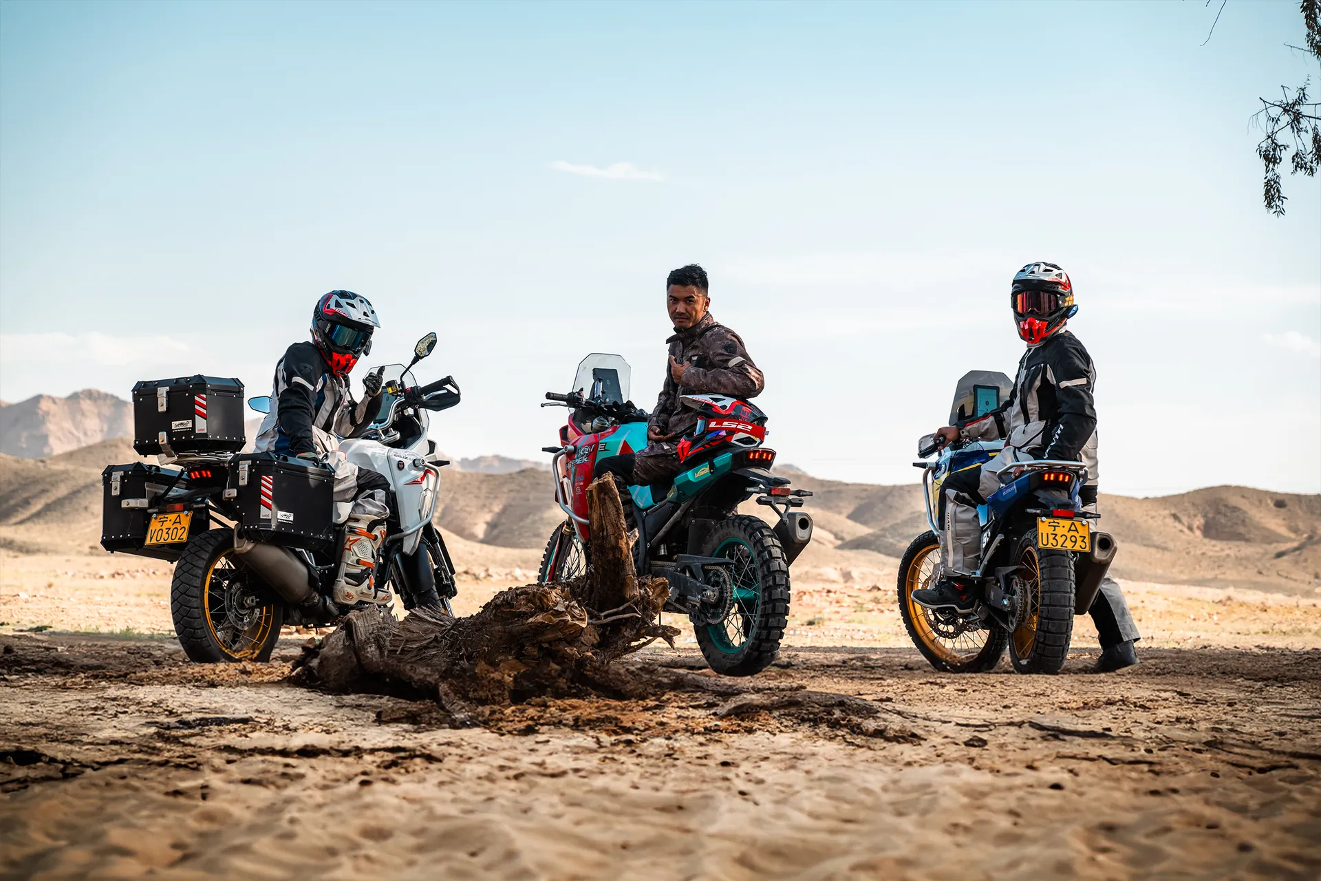 Tres motociclistas con equipo de aventura hacen un alto en un terreno árido, montados en motocicletas KOVE, con montañas de fondo.